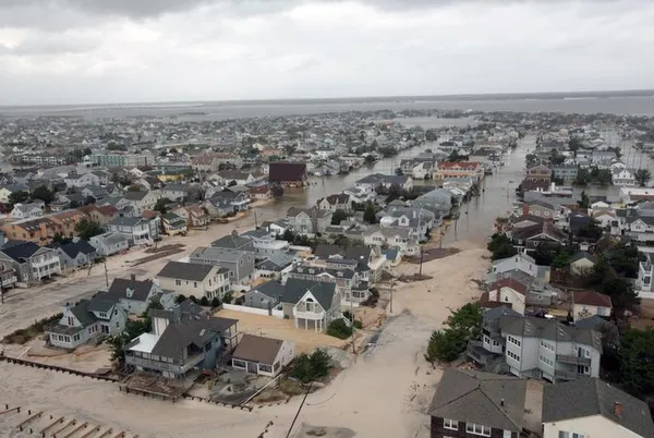 An aerial view of a neighborhood by the water with flooded streets, and mud and sand on roads on a gray day