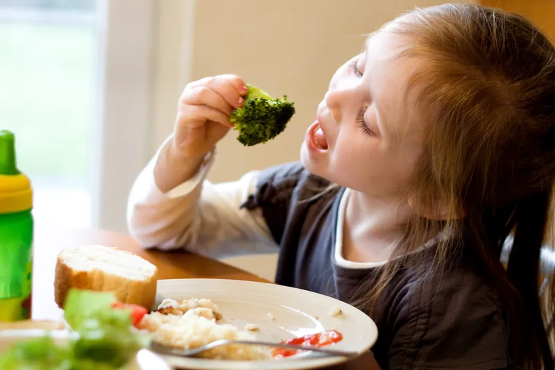 A girl eating broccoli.