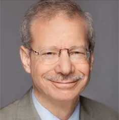 Headshot of an older white man with a mustache wears glasses and a suit.