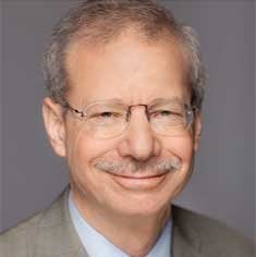 Headshot of an older white man with a mustache wears glasses and a suit.