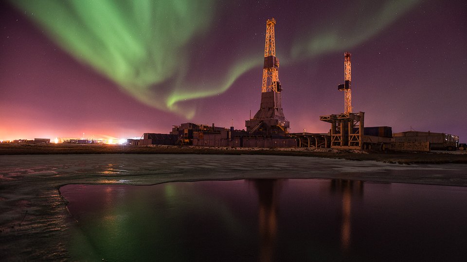 Oil towers and oil infrastructure in the arctic at night. The green waves of aurora borealis are in the night sky.