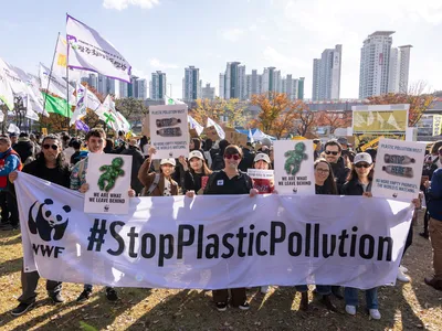 A group of people marching outdoors behind a banner that reads "#StopPlasticPollution"
