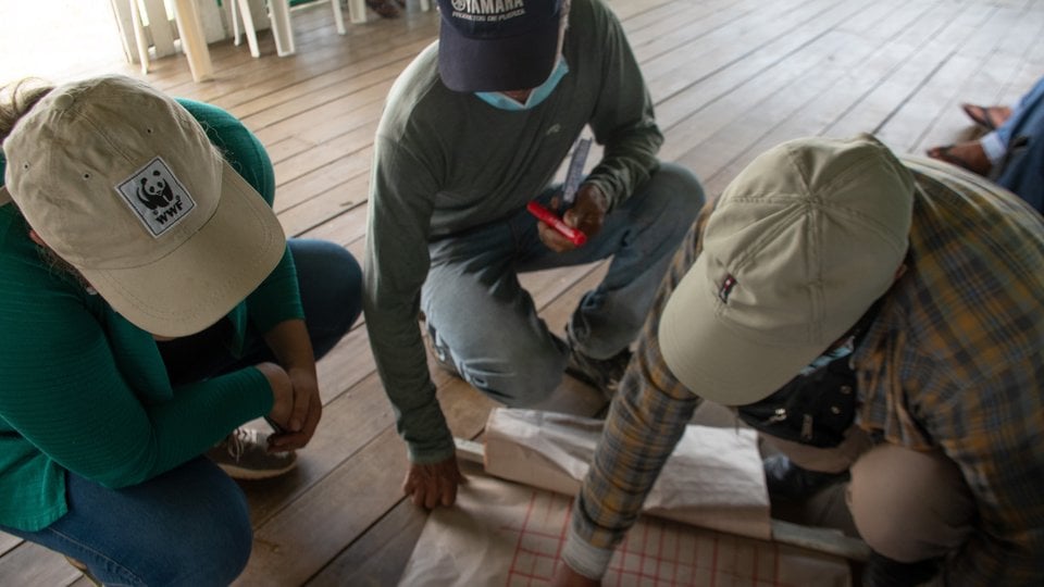 Three people hover over a document as they discuss livestock production and regenerative ranching in Madre de Dios region of Peruvian Amazon