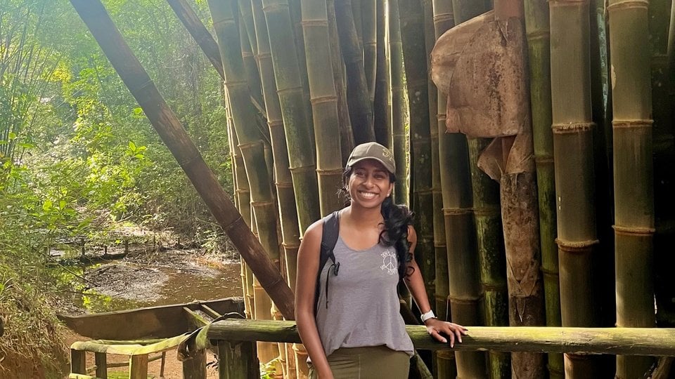 A color photo showing Sanjana Ramesh standing on a path in front of large bamboo