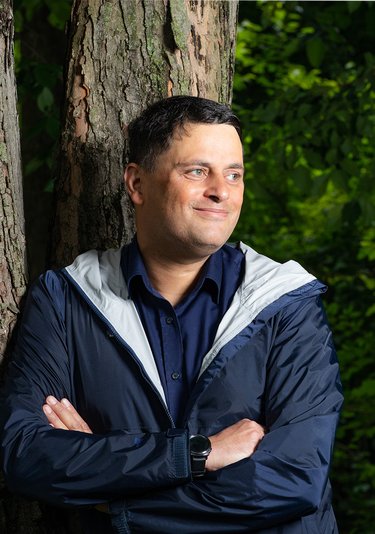 A man smiles while leaning against a tree