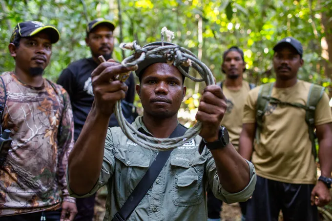 Merapi Mat Razi (centre) hBolds up a snare a snare found in Royal Belum State Park, Malaysia.