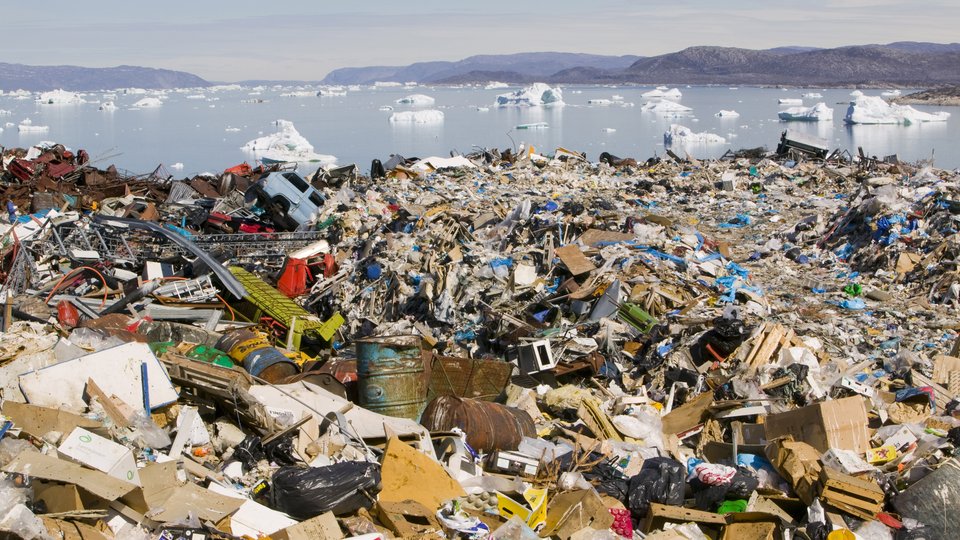 A massive landfill in the foreground, while icebergs float in a lake with mountains in the background.