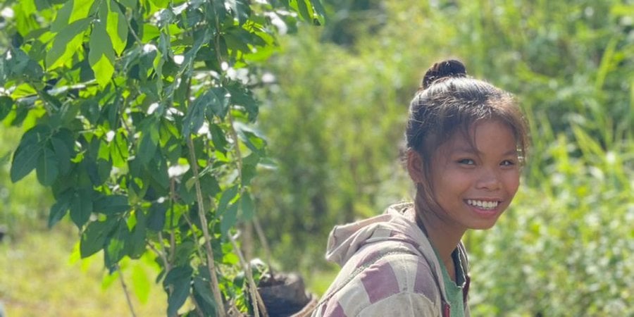 Young girl carrying seedling on her back and smiling in Laos